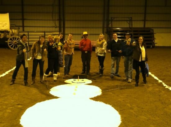 11 horseshoe players stand around a giant snowman made of flour in the indoor arena during the first annual Christmas Horseshoe Tournament