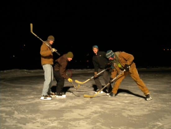 4 C Lazy U Ranch boys play hockey at night, on the freshly zambonied pond