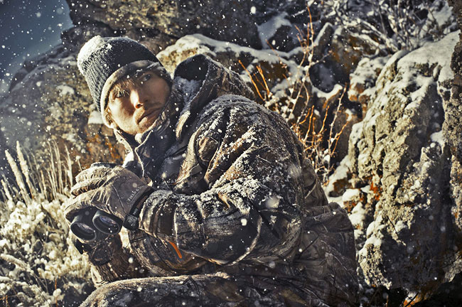 Paul poses in camo, binoculars ready, as snow falls around him.