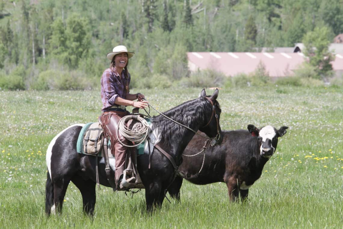 girl riding horse next to cow