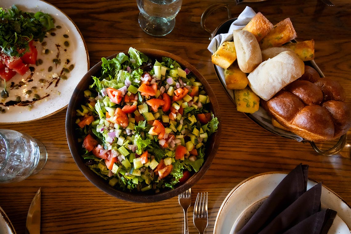 Chopped salad and assorted dinner rolls on a wooden table.