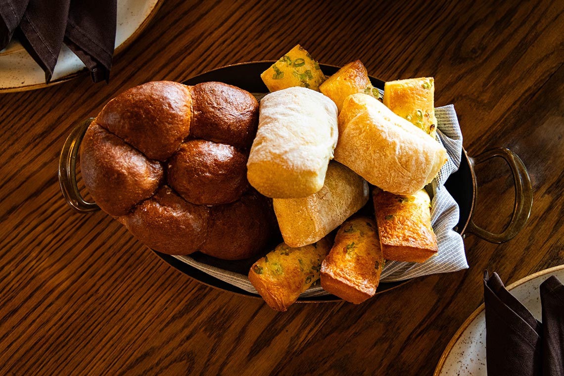 A bowl of handmade rolls and breads on a wooden table.