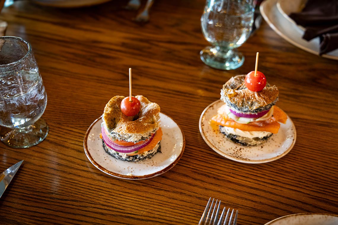 Mini sandwich appetizers with smoked salmon, red onion, and cucumber on small plates.
