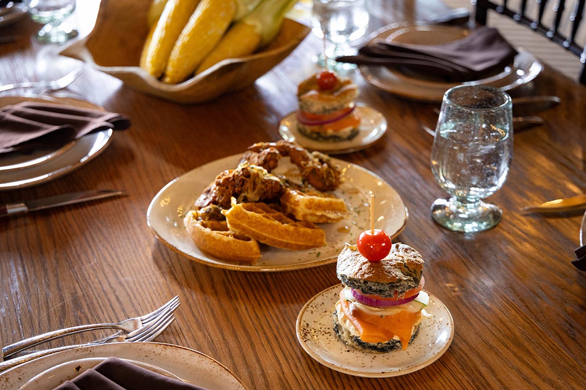 Table setting with mini sandwich appetizers, roasted chicken, and potato wedges.