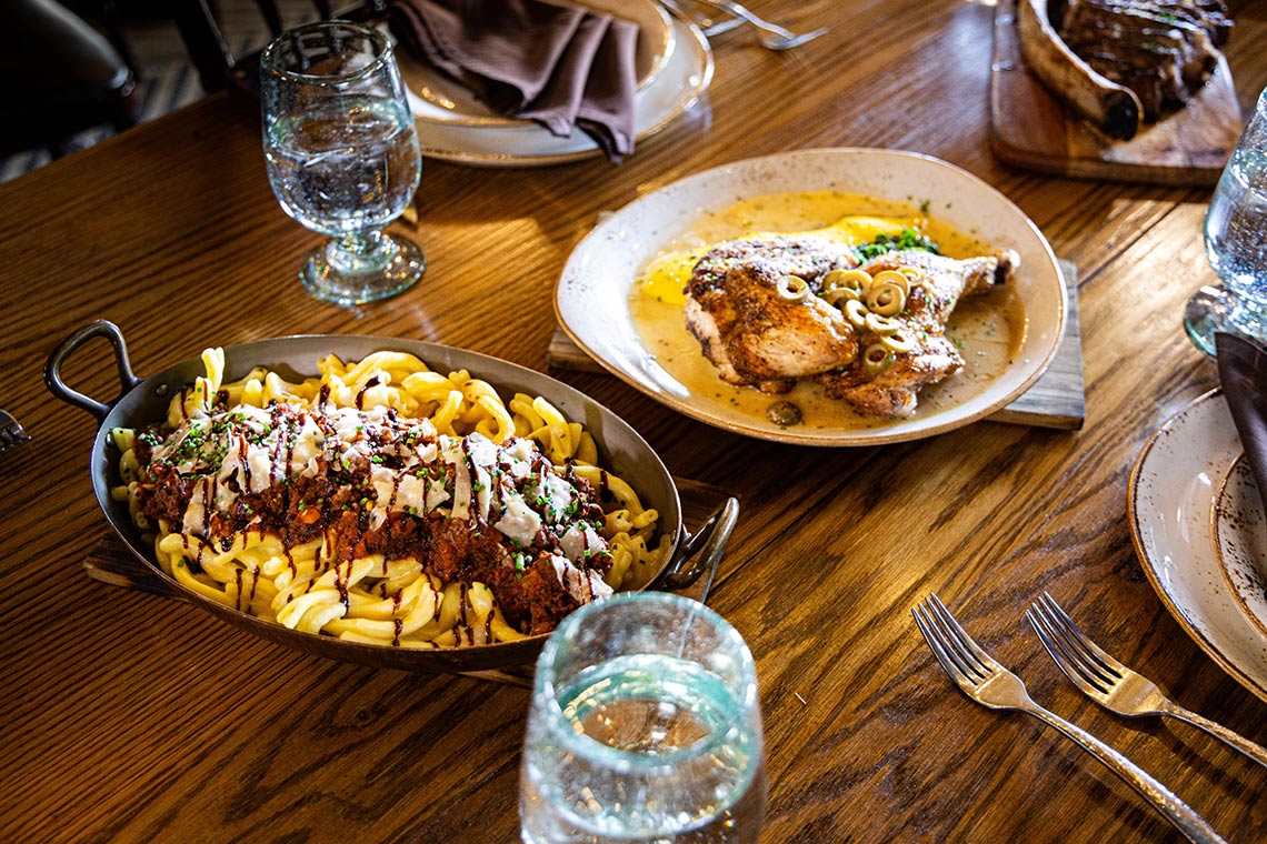 A pasta dish and a bowl of chicken legs set out for dining on a wooden table.