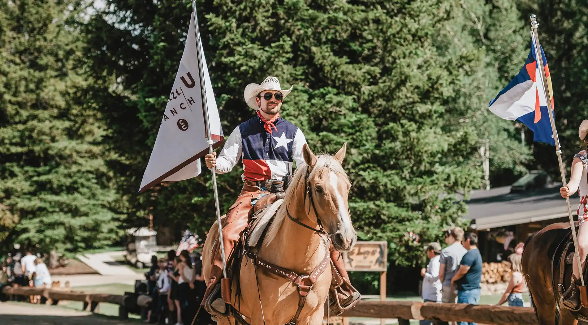 a wrangler rides a horse while carrying the C Lazy U flag