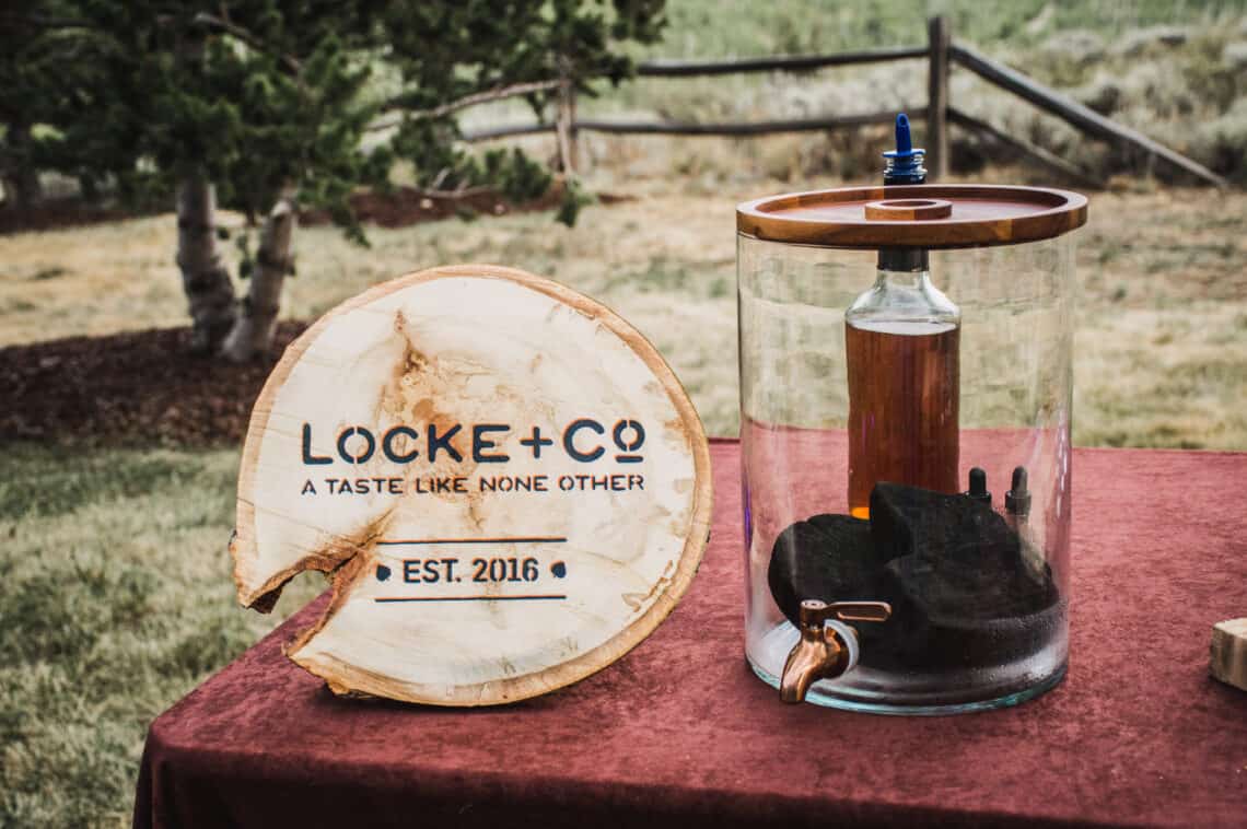 Lock + Co branded Aspen disc sits next to whiskey and charred aspen wood