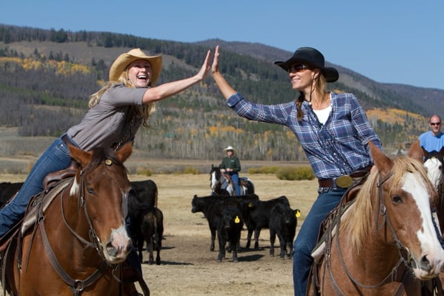 2 ladies on horses high-fiving