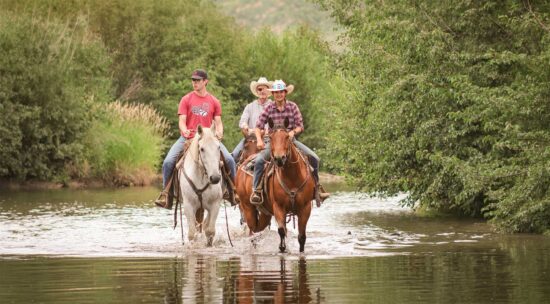 3 adults riding horses down Willow Creek during summer at C Lazy U Ranch