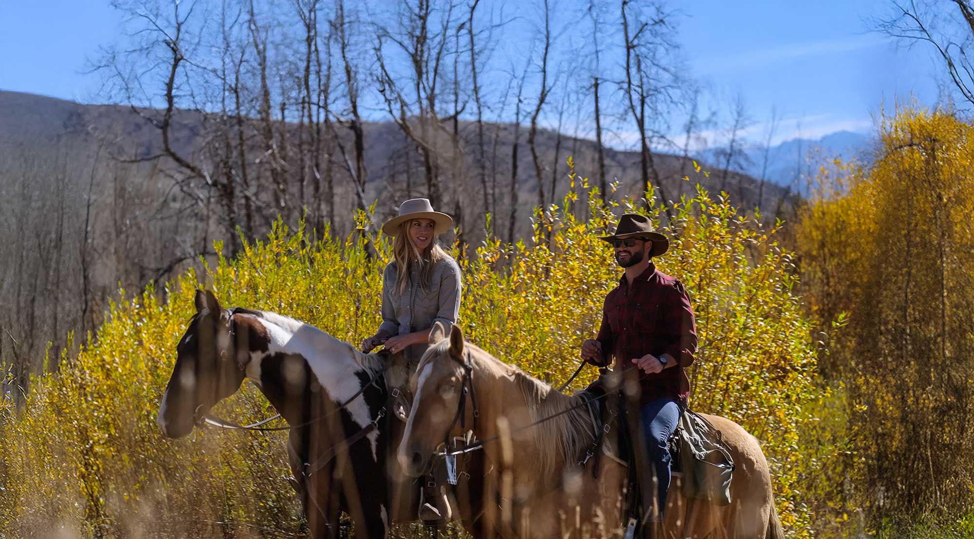 a man and woman riding horses in the fall and smiling