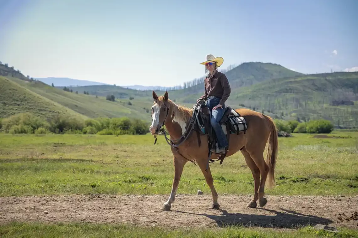 A girl riding a horse in the sunshine of the rocky mountains