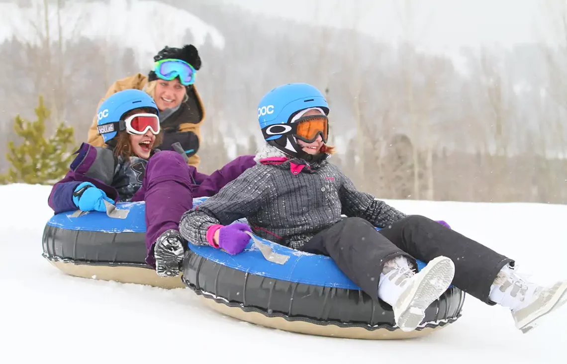 A kids' counselor gives two girls a push down the snowtubing hill