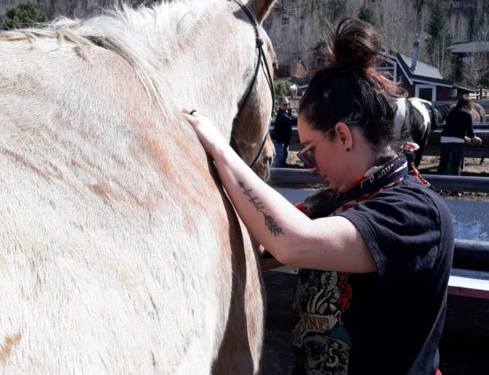 A participant grooms her horse during their Colorado summer vacation at C Lazy U Ranch