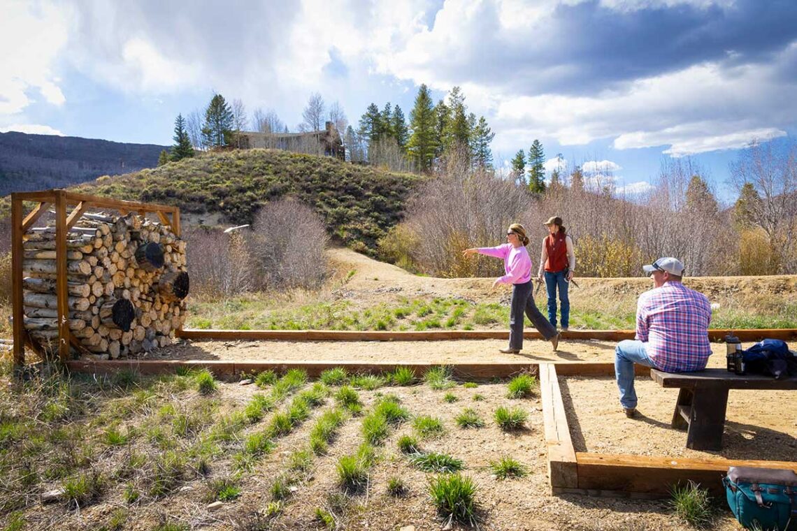 a woman throwing hatchets at wooden targets while a man waits his turn on a bench.