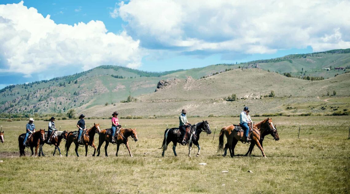 Adults ride horses in early spring at C Lazy U Ranch