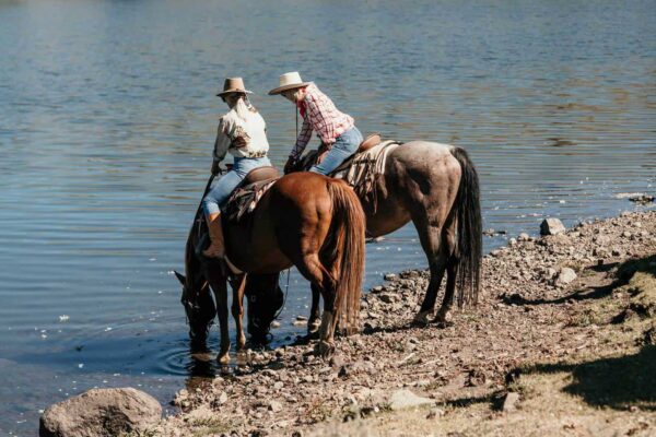 Two women on horses let the horses drink from the lake