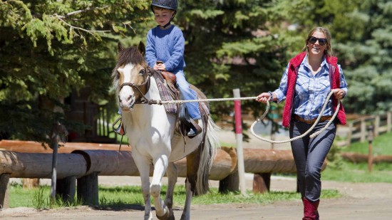 Small child enjoying a pony ride during their vacation at C Lazy U