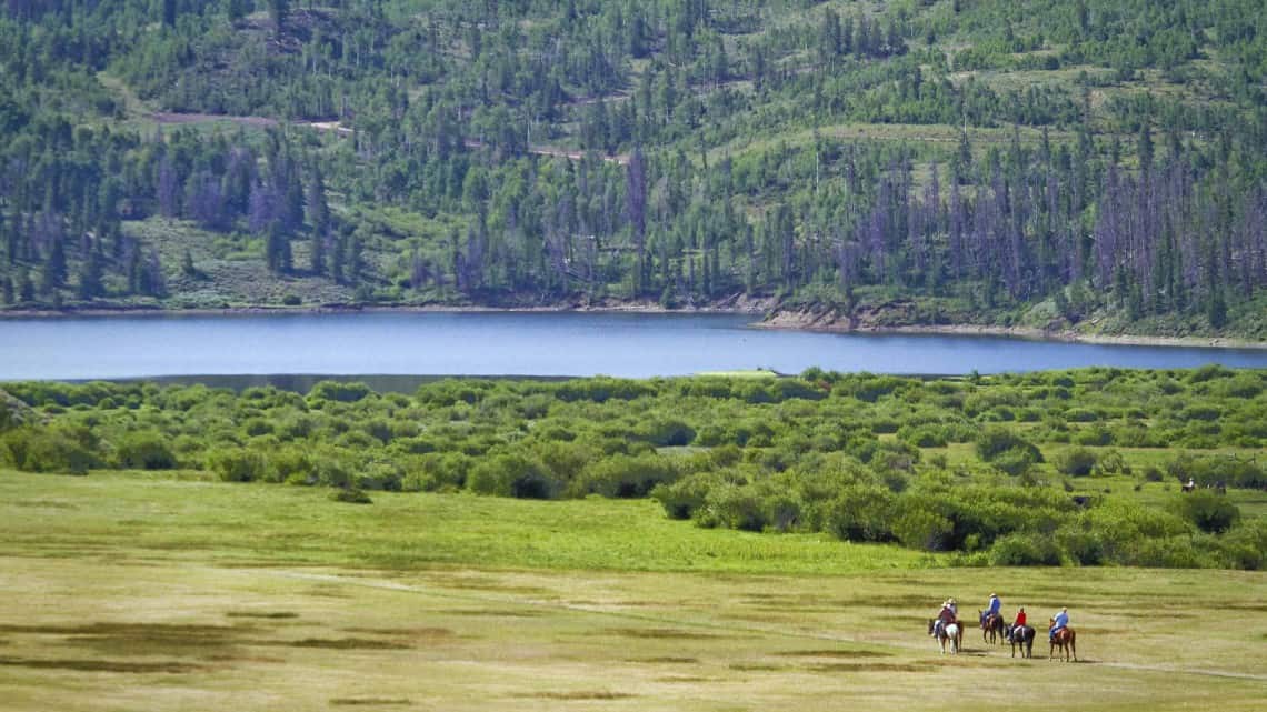 aerial drone view of 4 tiny horseback riders approaching the reservoir