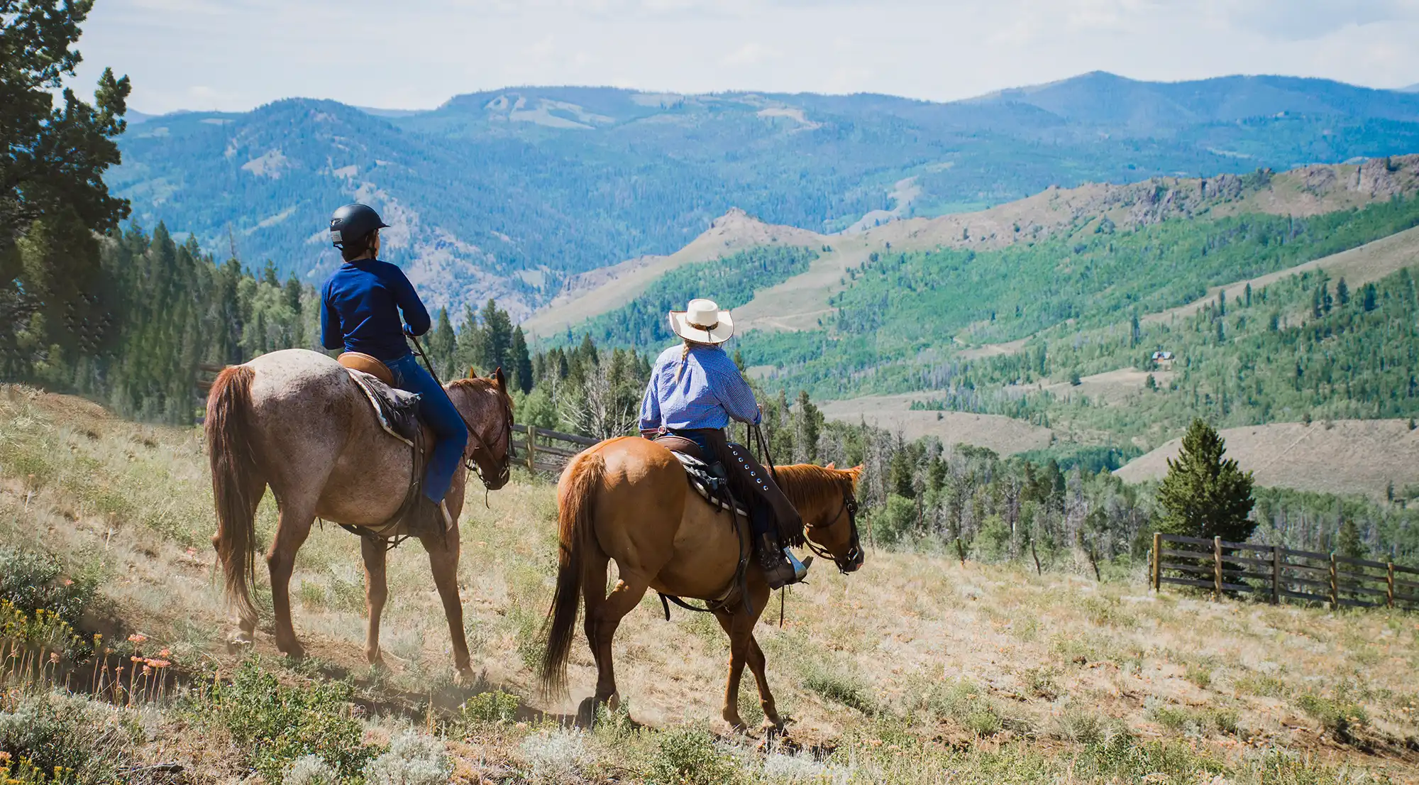 A child and an adult guide ride horses in the mountains at C Lazy U Ranch