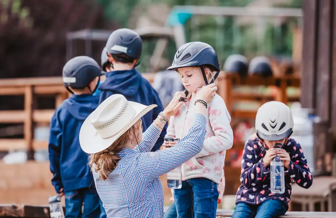 counselor adjusting a helmet on a child about to go for a horseback ride