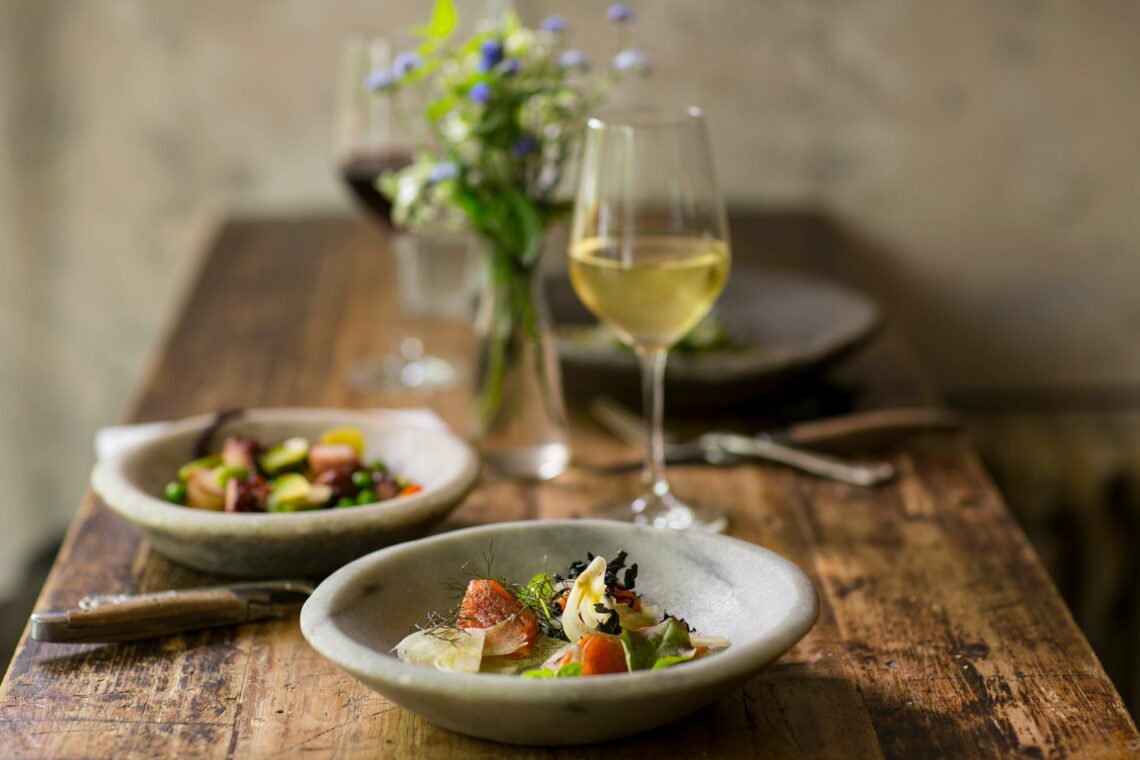 White wine glass sits near upscale cuisine on a wooden table