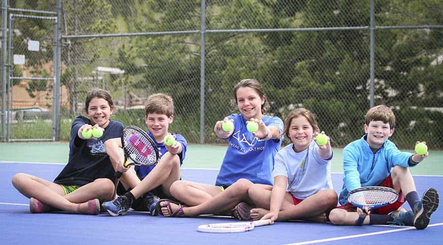 Kid sitting on tennis court holding tennis balls