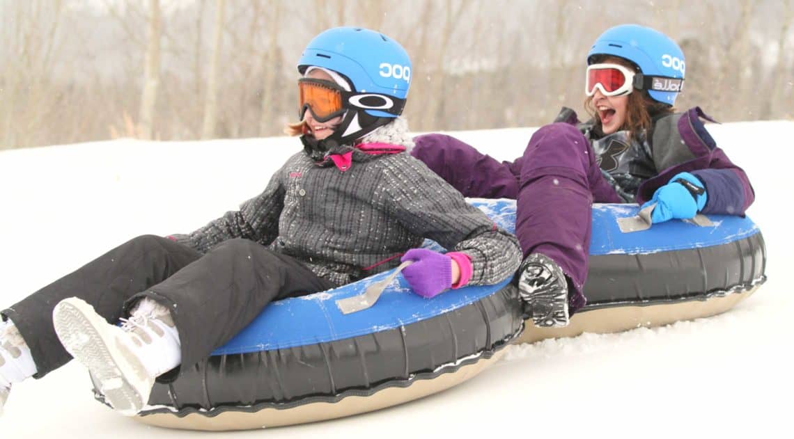 Two girls snowtubing during a winter getaway vacation at C Lazy U