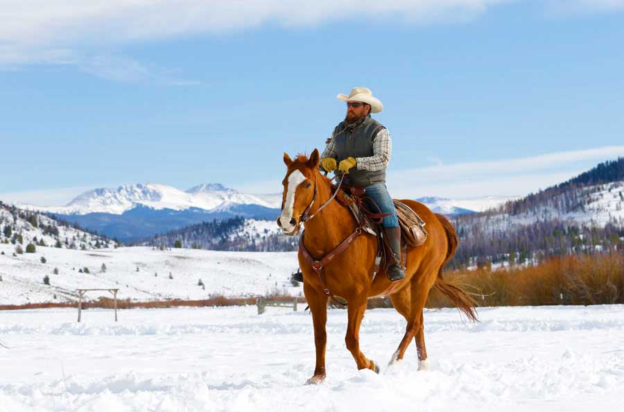 A dude ranch guest rides his horse through the snow.