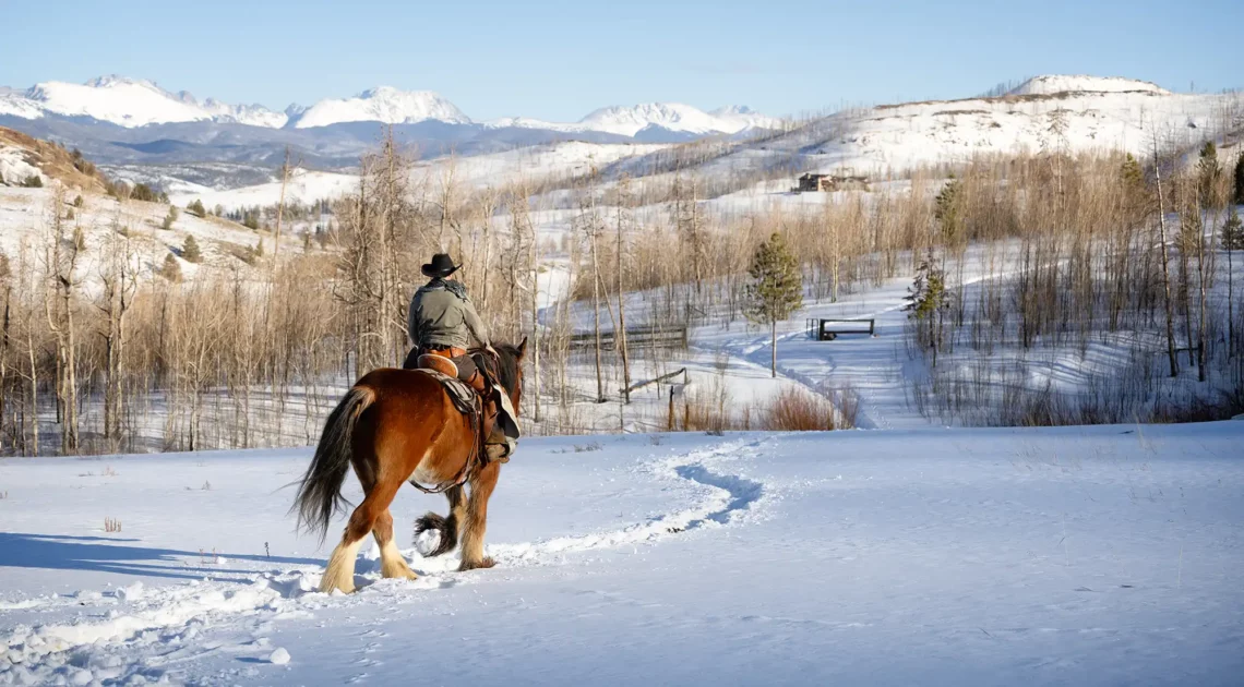 A lone cowboy rides out into the winter landscape on his horse