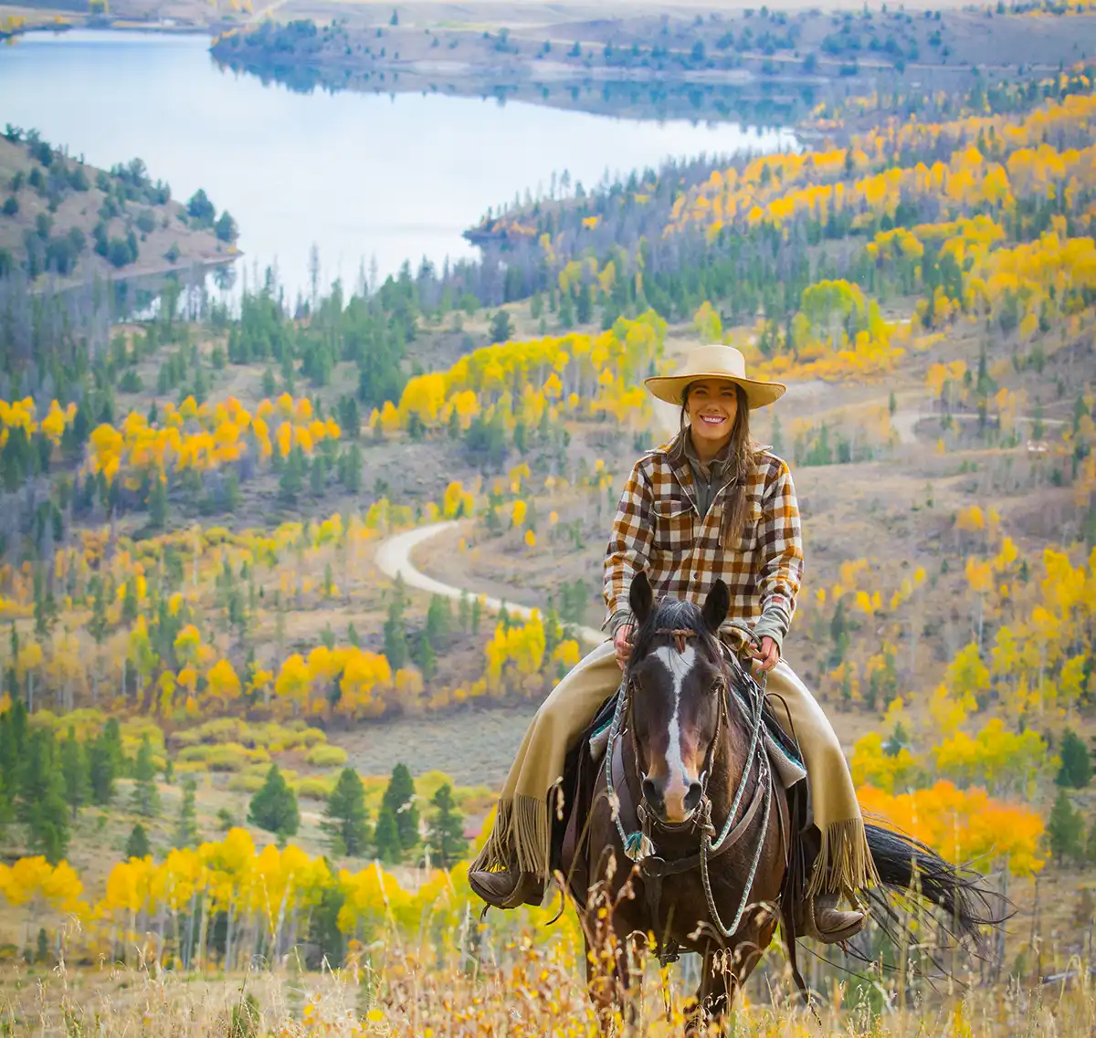 woman riding horse in fall Woman riding up a hill in the fall at C Lazy U ranch. A view of the reservoir and mountains behind her.